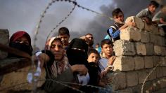 Newly displaced people wait as they complain about what they say is a lack of humanitarian aid outside the processing center in Qayyara