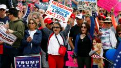 Women carry signs with pro-Trump rally participants  during the Southern California Make America Great Again march in support of President Trump, the military and first responders at Bolsa Chica State Beach in Huntington Beach, California