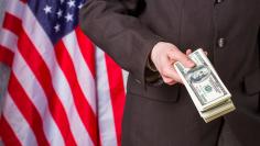 Businessman holding dollars beside flag.