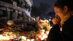 A woman weeps as she kneels near bouquets of flowers and burning candles at the Place de la Republique in Paris