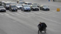 A man rides a tricycle past vehicles through a junction in Beijing