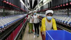 FILE PHOTO: A worker jokes and beckons at her colleague as she rolls away carts of unused tools between rows of spinning machine at a factory owned by Hong Kong's Novetex Textiles Limited in Zhuhai City, Guangdong Province, China December 13, 2016.  REUT