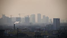 FILE PHOTO: File photo of smoke rising from a chimney among houses as new high-rise residential buildings are seen under construction on a hazy day in the city centre of Tangshan