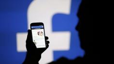 A man is silhouetted against a video screen with an Facebook logo as he poses with an Samsung S4 smartphone in this photo illustration taken in the central Bosnian town of Zenica, August 14, 2013. REUTERS/Dado Ruvic/File Photo