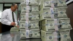 An employee of the Korea Exchange Bank works next to stacks of one hundred dollar notes at the bank's headquarters in Seoul