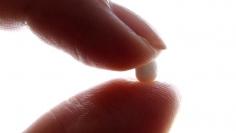 An illustration picture shows a woman holding a pill at her home in Nice