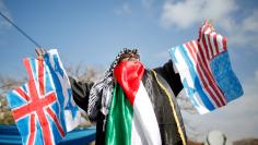 Palestinian demonstrator gestures as he holds representations of Israeli, British and U.S. flags before burning them during a protest against a U.S. decision to cut aid, in Gaza City