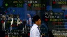 A man walks past a display of the Nikkei average and other market indices outside a brokerage in Tokyo, Japan April 19, 2016. REUTERS/Thomas Peter  