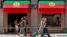 FILE PHOTO: People walk past a shop decorated with Portugal's national flags in downtown Lisbon