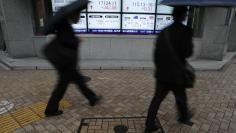 Pedestrians with umbrellas walk past an electronic board showing Japan's Nikkei average (top middle L) and the exchange rates between the Japanese yen and the U.S. dollar (top middle R), outside a brokerage in Tokyo November 11, 2014. REUTERS/Yuya Shino 