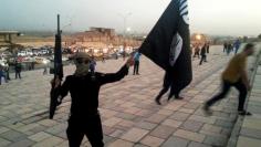 A fighter of ISIL holds a flag and a weapon on a street in Mosul