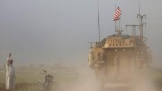 FILE PHOTO - A man gestures at U.S military vehicles driving in the town of Darbasiya next to the Turkish border, Syria April 28, 2017. REUTERS/Rodi Said 