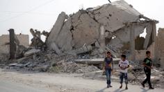 Boys walk past damaged buildings in Bizaah, northeast of Aleppo's countryside, Syria September 16, 2017. Picture taken September 16, 2017. REUTERS/Khalil Ashawi