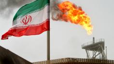 A gas flare on an oil production platform in the Soroush oil fields is seen alongside an Iranian flag in the Gulf July 25, 2005. REUTERS/Raheb Homavandi/File Photo