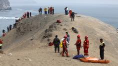 Rescue workers stand next to victims after a bus crashed with a truck and careened off a cliff along a sharply curving highway north of Lima