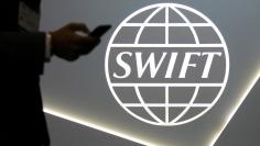 FILE PHOTO: A man using a mobile phone passes the logo of global secure financial messaging services cooperative SWIFT at the SIBOS banking and financial conference in Toronto