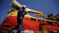 FILE PHOTO:  A worker carries construction materials as he walks past a ship which is currently under construction at Hyundai Heavy Industries' Shipyard in Ulsan, South Korea