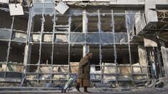 A woman pulls her shopping trolley as she walks past a building that was damaged by shelling in Donetsk, eastern Ukraine in this October 15, 2014 file photo. REUTERS/Shamil Zhumatov/Files 