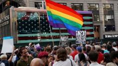 FILE PHOTO: A rainbow flag flies as people protest U.S. President Donald Trump's announcement that he plans to reinstate a ban on transgender individuals from serving in any capacity in the U.S. military, in Times Square, in New York City, New York, U.S.