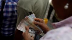 FILE PHOTO: A woman counts Venezuelan bolivar notes at a vegetable street market in Caracas, Venezuela November 13, 2017. REUTERS/Marco Bello