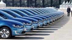 People walk past a row of Volkswagen e-Golf cars during the company's annual news conference in Berlin March 13, 2014.  REUTERS/Tobias Schwarz   