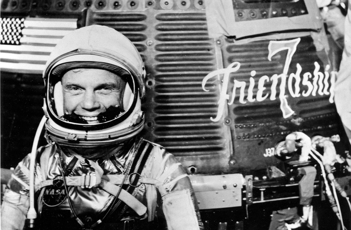 Astronaut John H. Glenn Jr. poses for a photo with the Mercury &quot;Friendship 7&quot; spacecraft at the Kennedy Space Center in Cape Canaveral