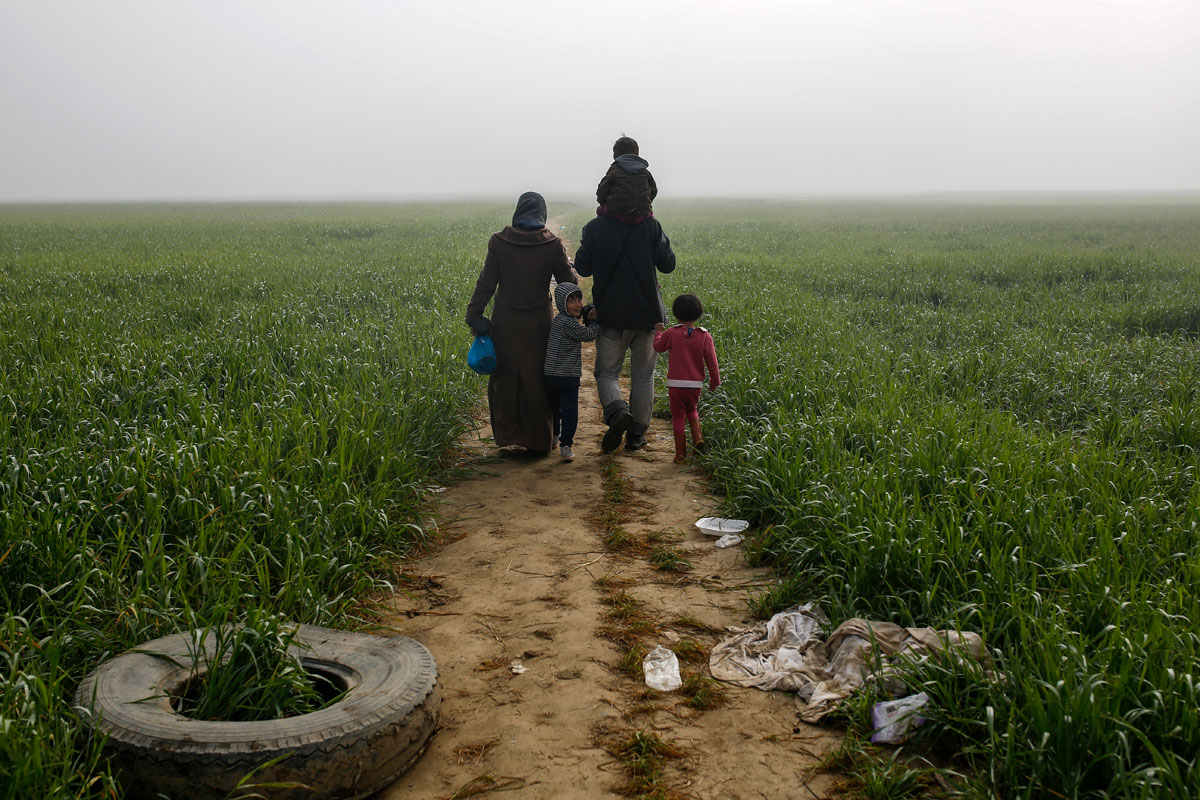 A family walks through a field at a makeshift camp for migrants and refugees at the Greek-Macedonian border near the village of Idomeni
