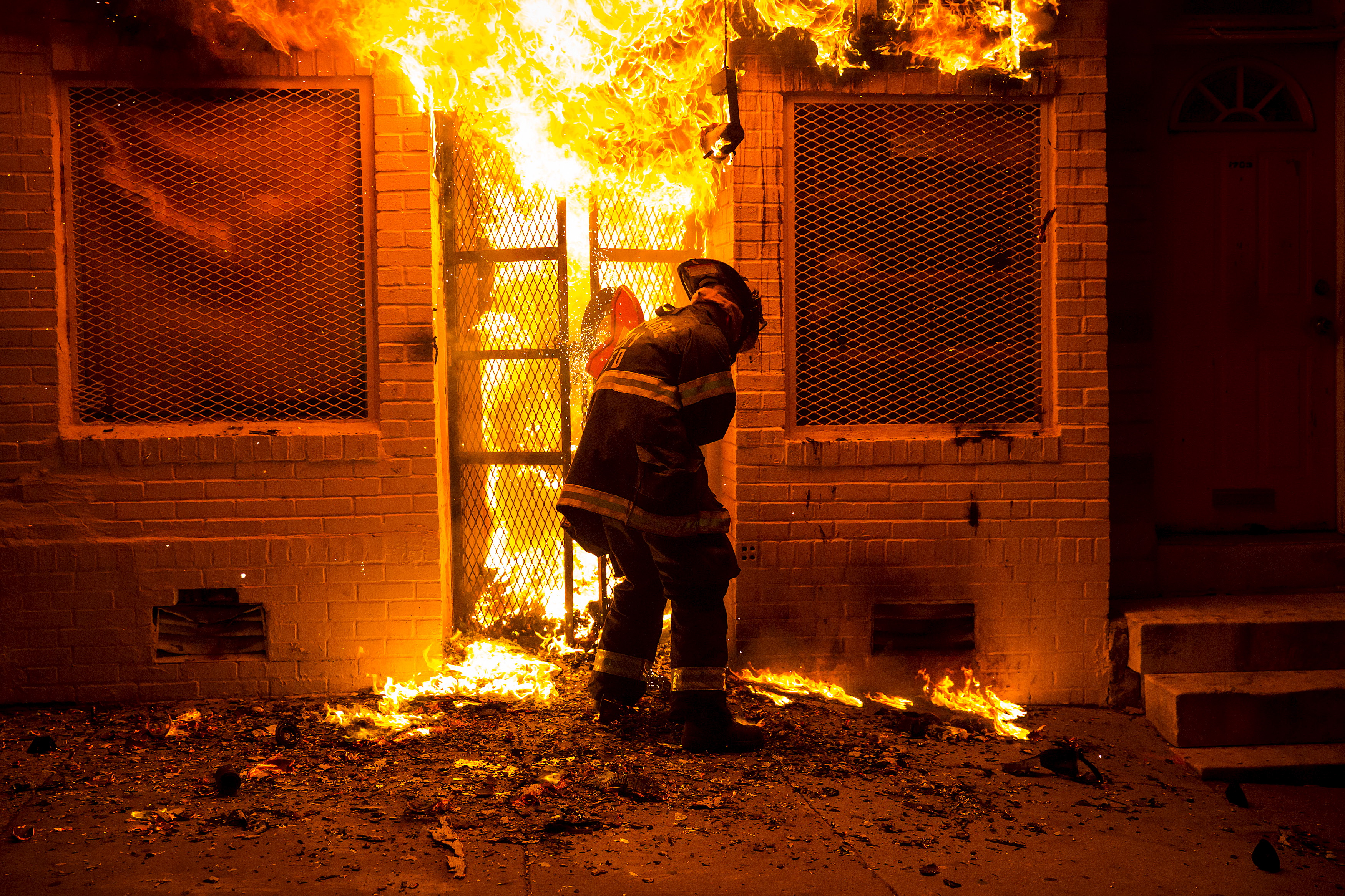A firefighter uses a saw to open a metal gate while fighting a fire in a convenience store and residence during clashes after the funeral of Freddie Gray in Baltimore, Maryland