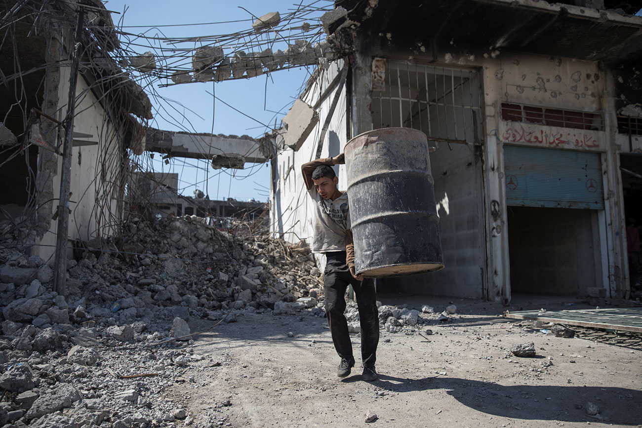 A man carries a barrel as people collect steel from a destroyed building in Mosul