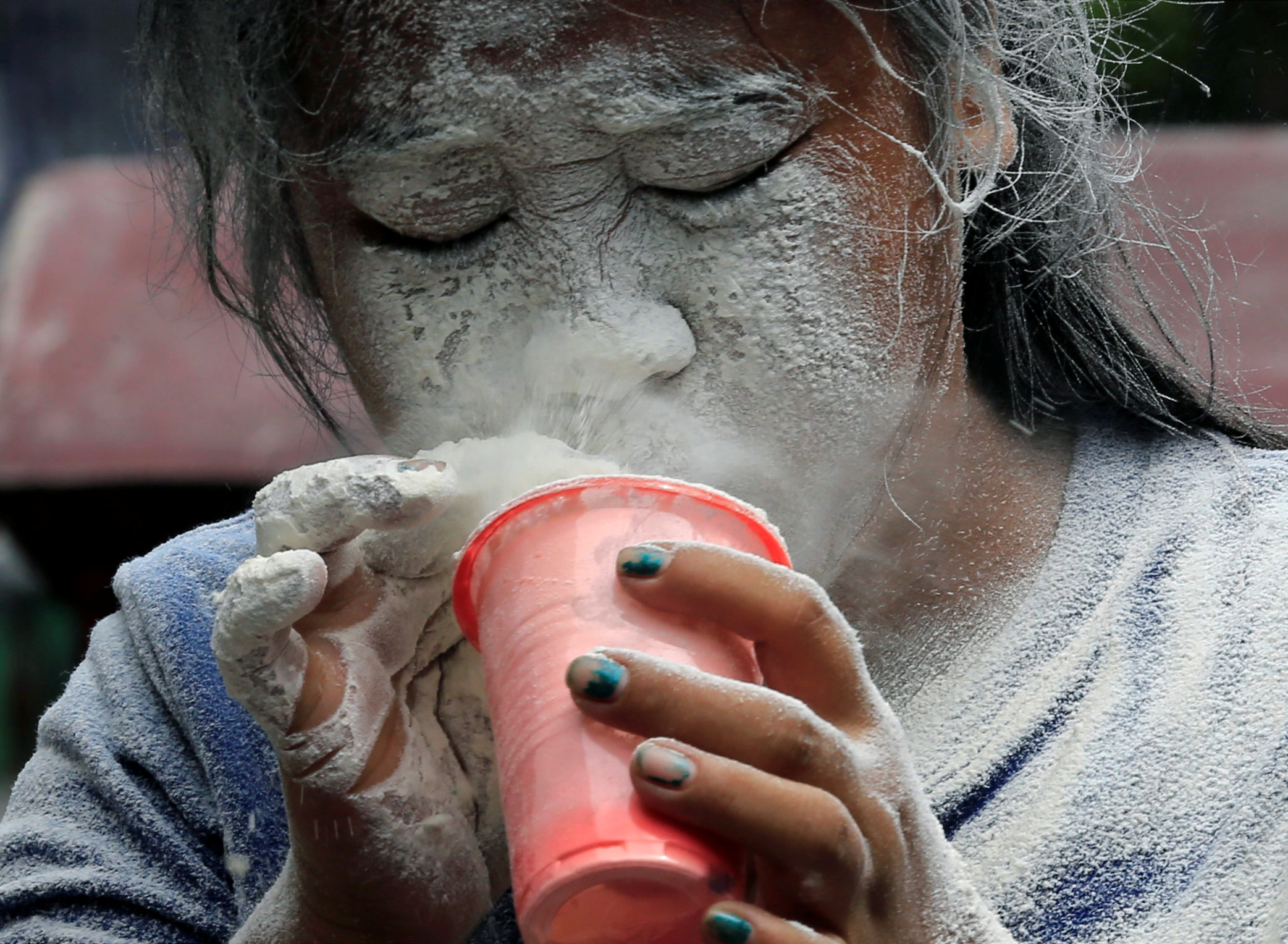 A girl&#039;s face is covered by a white powder after blowing on it, while participating in a game during a religious festival honouring patron saint Santa Rita de Cascia in Paranaque city