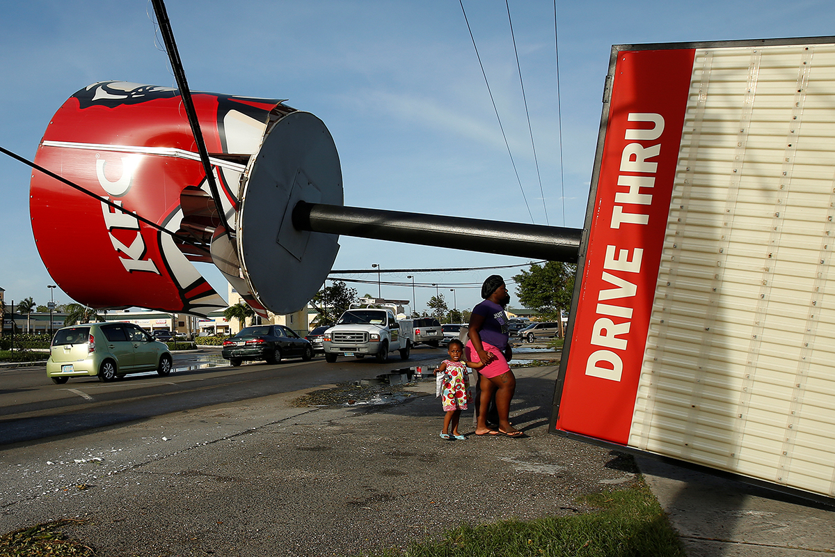 People walk under a broken Kentucky Fried Chicken sign that blew over in Hurricane Matthew in Nassau