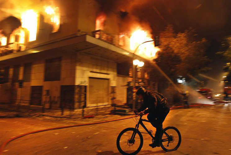 A cyclist rides past a burning building during violent protests in central Athens, February 12, 2012.
