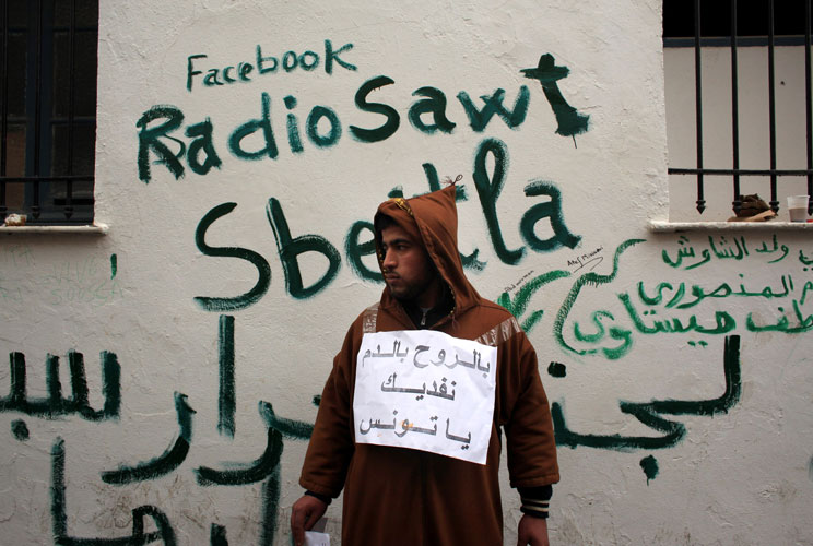 A man stands next to Facebook graffiti as Tunisians continued their demonstrations outside Prime Minister Mohammed Ghannouchi&#039;s offices in Government Square Tunis on January 25, 2011 in Tunis, Tunisia. The government square became a makeshift camp as prot