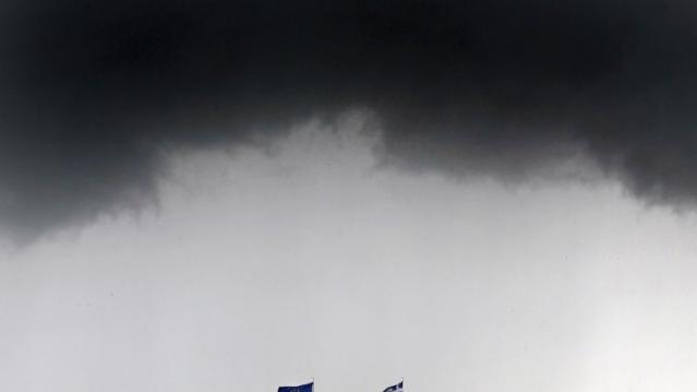 A Greek national flag and a European Union flag flutter under storm clouds in Athens May 28, 2015. REUTERS/Alkis Konstantinidis   