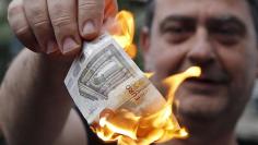 An anti-austerity protester burns a euro note during a demonstration outside the European Union (EU) offices in Athens