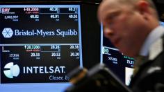 A trader passes by a screen displaying the tickers symbols for Bristol-Myers Squibb and Intelsat, Ltd. on the floor at the New York Stock Exchange