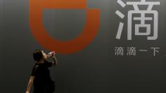 FILE PHOTO: A woman walks past Didi Chuxing's booth at the GMIC in Beijing