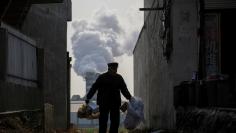 FILE PHOTO: Man collects recyclables from an alley as smoke billows from the chimney of a factory in rural Gaoyi county near Shijiazhuang