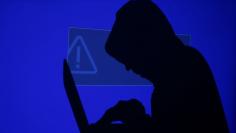 A hooded man holds a laptop computer as blue screen with an exclamation mark is projected on him in this illustration picture taken on May 13, 2017. REUTERS/Kacper Pempel/Illustration 