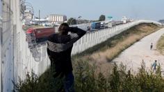 Migrant walks past the fence which secures the approach to the city from migrants trying to reach Britain, in Calais