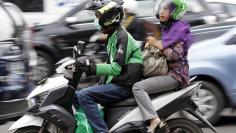 FILE PHOTO: Woman rides on the back of a motorbike, part of the Go-Jek ride-hailing service, on a busy street in central Jakarta