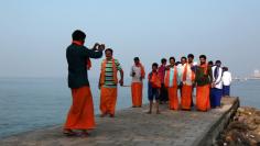 A group of domestic tourists is photographed by a fellow tourist as they stand on a promenade at Fort Kochi beach