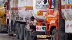 FILE PHOTO: A driver reads a newspaper as he sits on a spare tire attached to a parked oil tanker at a truck terminal in Mumbai