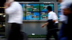 People walk past an electronic board showing Japan's Nikkei average outside a brokerage at a business district in Tokyo, Japan August 9, 2017.   REUTERS/Kim Kyung-Hoon 