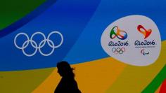 A journalist walks in front of a screen with olympics logos during the medal launching ceremony in Rio de Janeiro