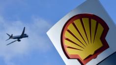 A passenger plane flies over a Shell logo at a petrol station in west London, in this January 29, 2015 file photo. REUTERS/Toby Melville/Files      