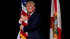 Trump hugs a U.S. flag as he comes onstage to rally with supporters in Tampa, Florida