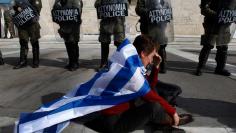 An anti-austerity protester draped with a Greek flag sits in front of police guarding parliament in Athens February 11, 2012 during a demonstration on the second day of a 48-hour strike by Greek workers unions.