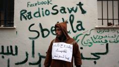 A man stands next to Facebook graffiti as Tunisians continued their demonstrations outside Prime Minister Mohammed Ghannouchi's offices in Government Square Tunis on January 25, 2011 in Tunis, Tunisia. The government square became a makeshift camp as prot